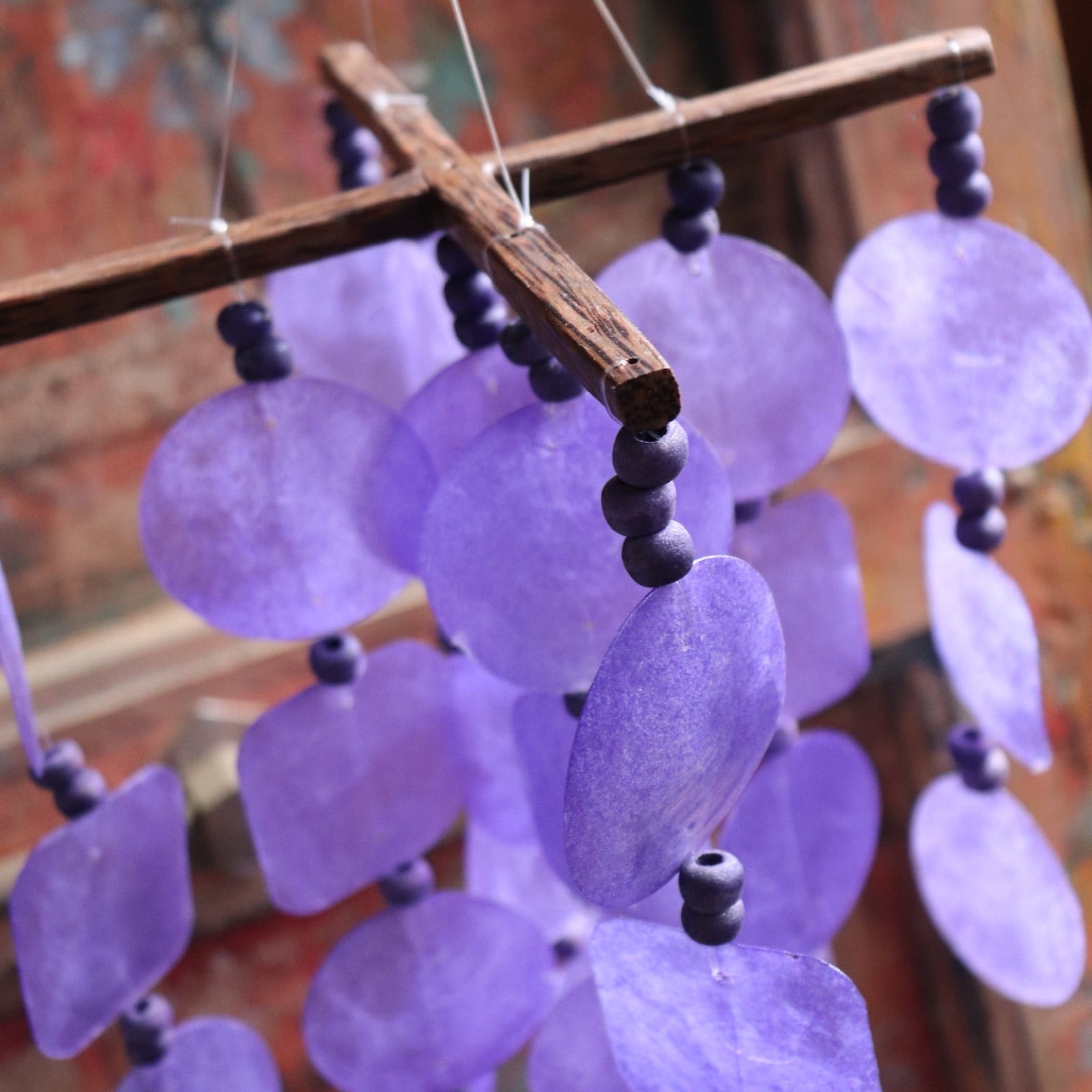 An up-close image of the Purple Capiz Chime in front of a wooden door.