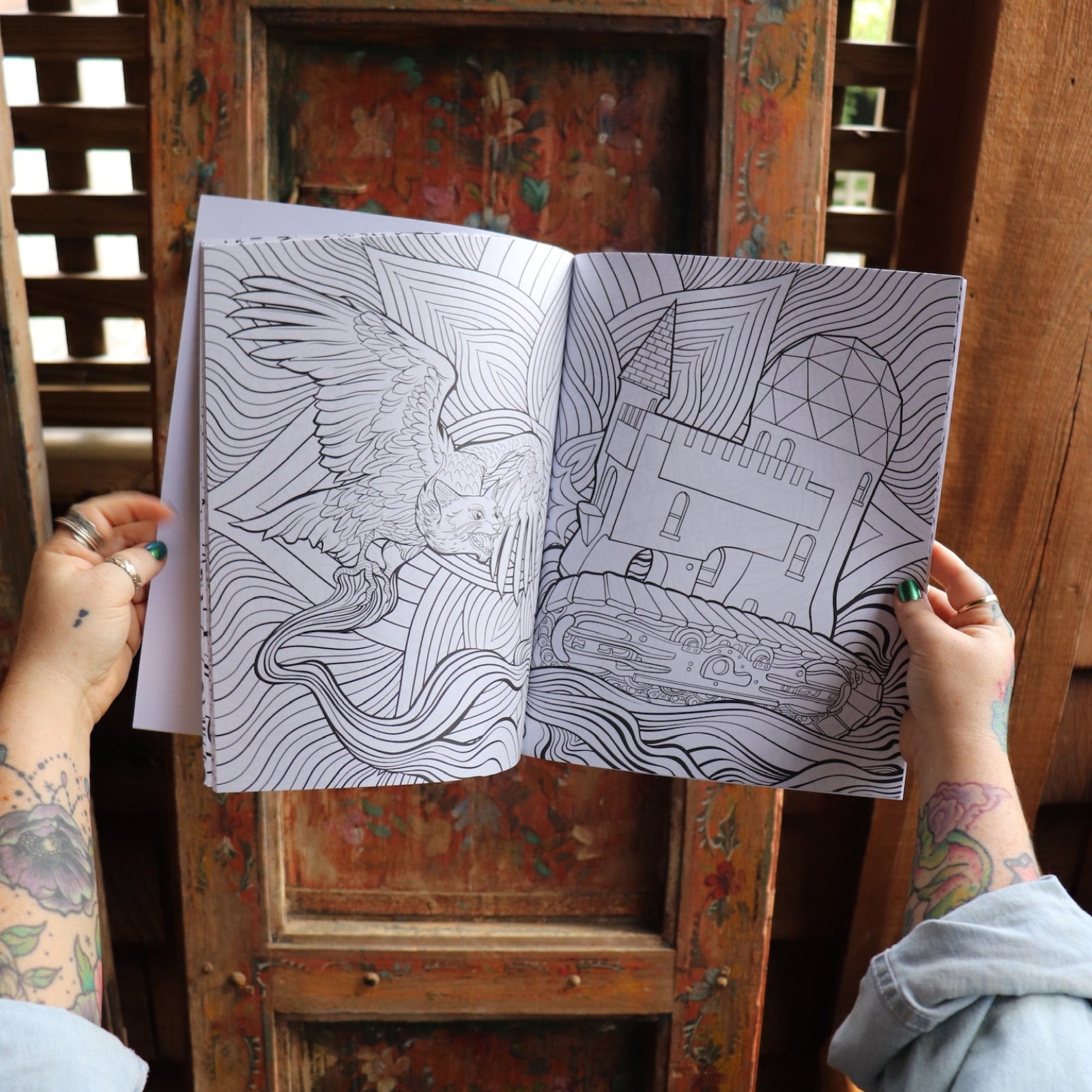 Someone holding the Psychedelic Cats Coloring Book open in front of a wooden background, showing off the pages.