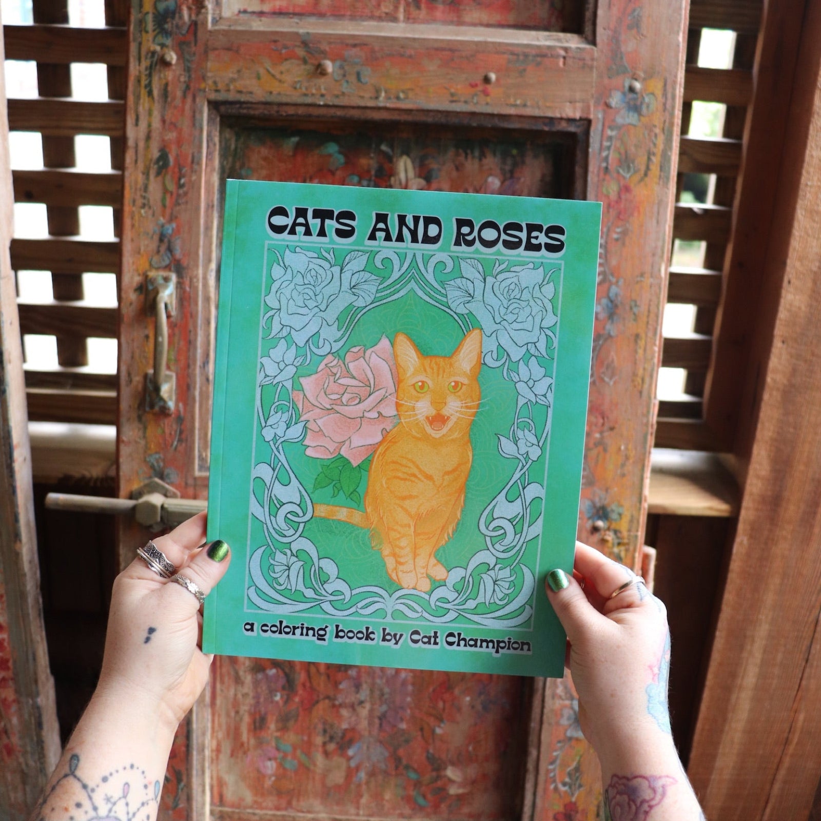 Someone holding the Cats and Roses Coloring Book in front of a wooden background.