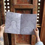 Someone holding the Cats and Roses Coloring Book open in front of a wooden background, showing off the pages.