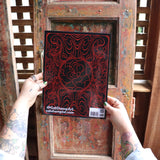 Someone holding the Cats and Roses Coloring Book in front of a wooden background, showing off the back.