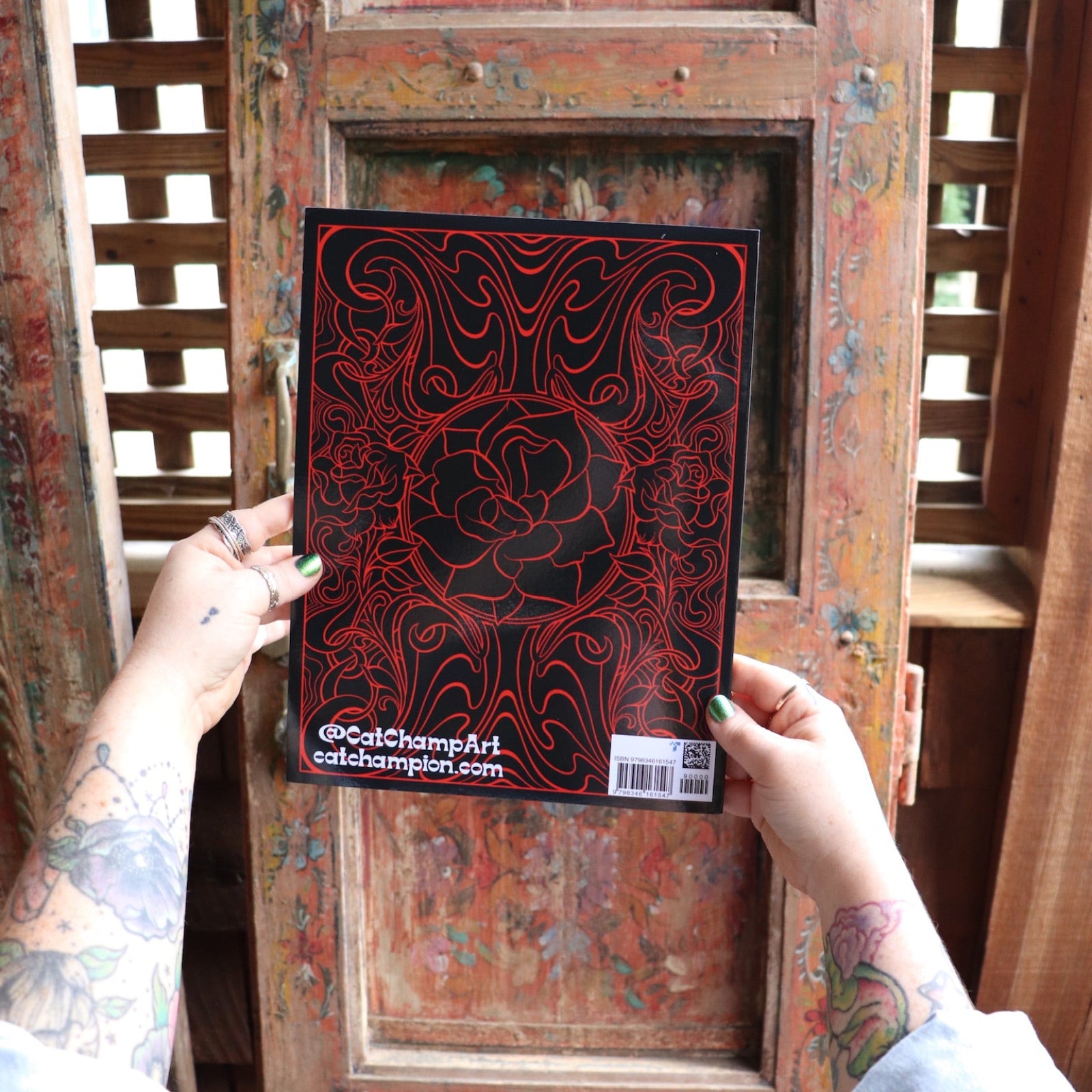 Someone holding the Cats and Roses Coloring Book in front of a wooden background, showing off the back.