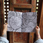 Someone holding the Stoner Cats Coloring Book open in front of a wooden background, showing off the pages.