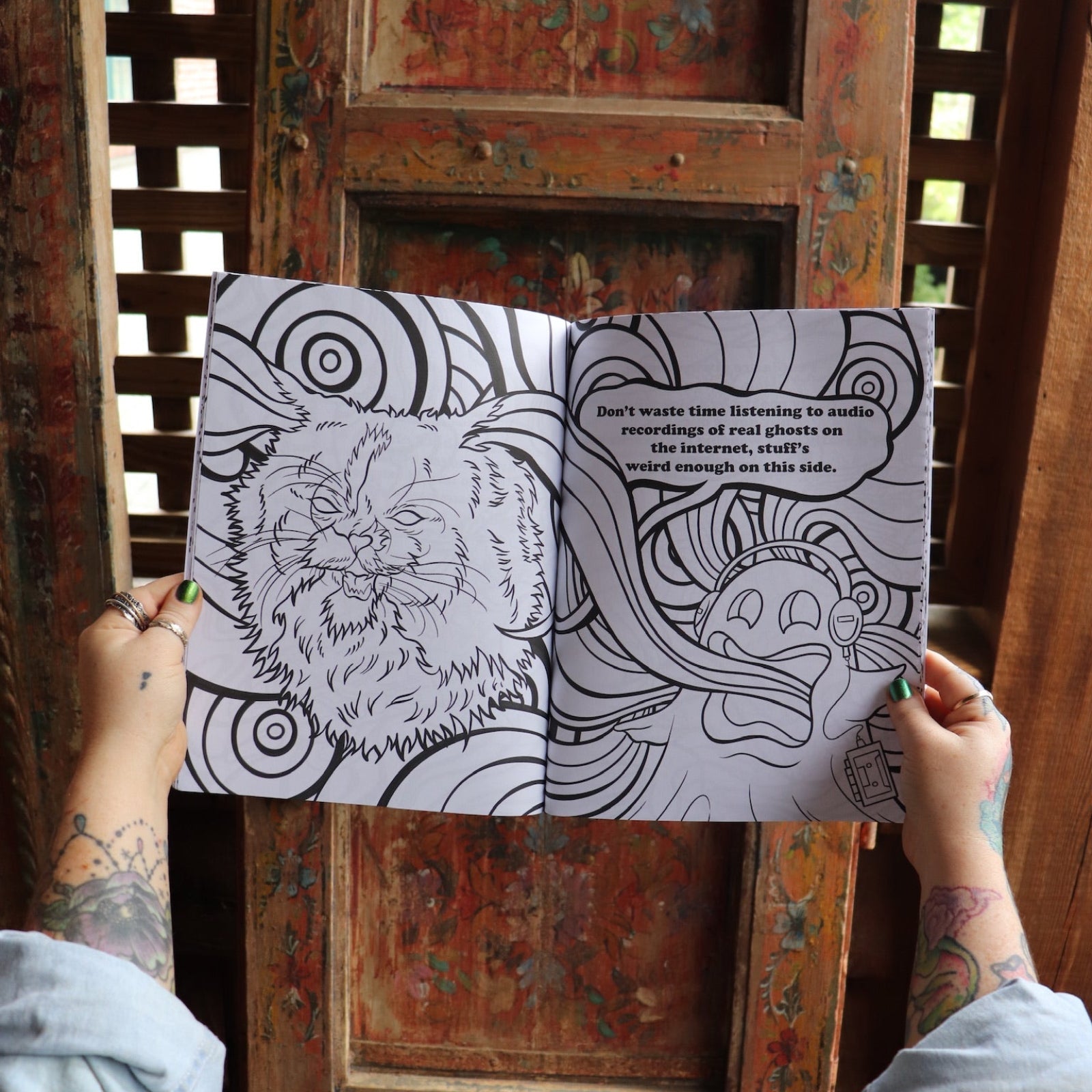 Someone holding the Stoner Cats Coloring Book open in front of a wooden background, showing off the pages.