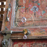 Someone holding the Prisma Hanging #22 Brass Round Suncatcher in front of a wooden background.