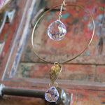 An up-close image of someone holding the Prisma Hanging #22 Brass Round Suncatcher in front of a wooden background.