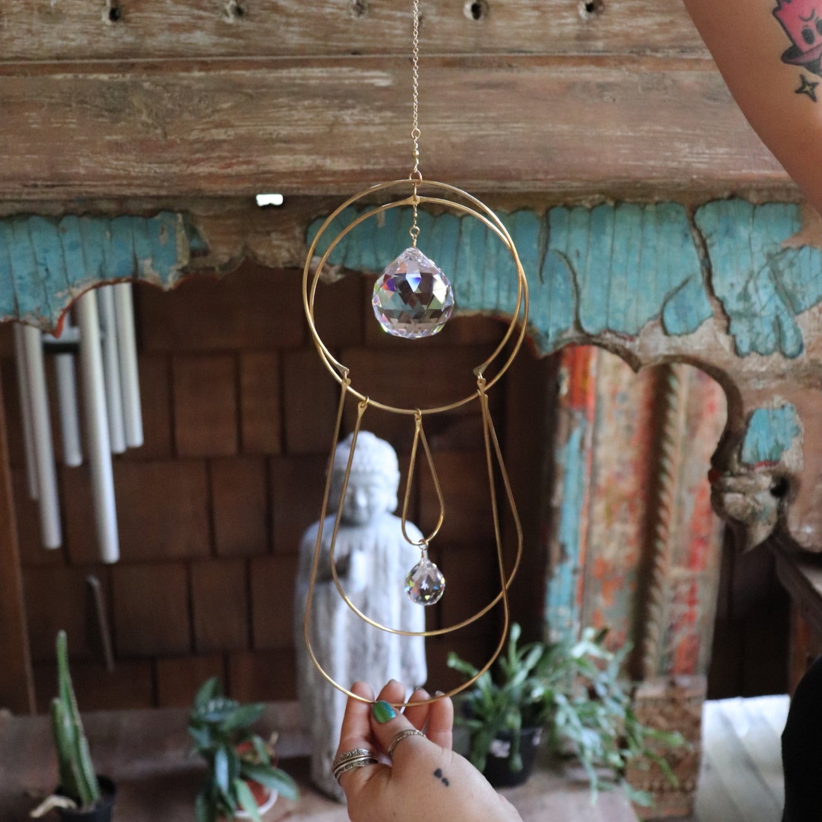 Someone holding the Prisma Hanging #43 Brass Suncatcher in front of a wooden altar.