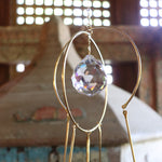 Someone holding the Prisma Hanging #43 Brass Suncatcher in front of a wooden altar.