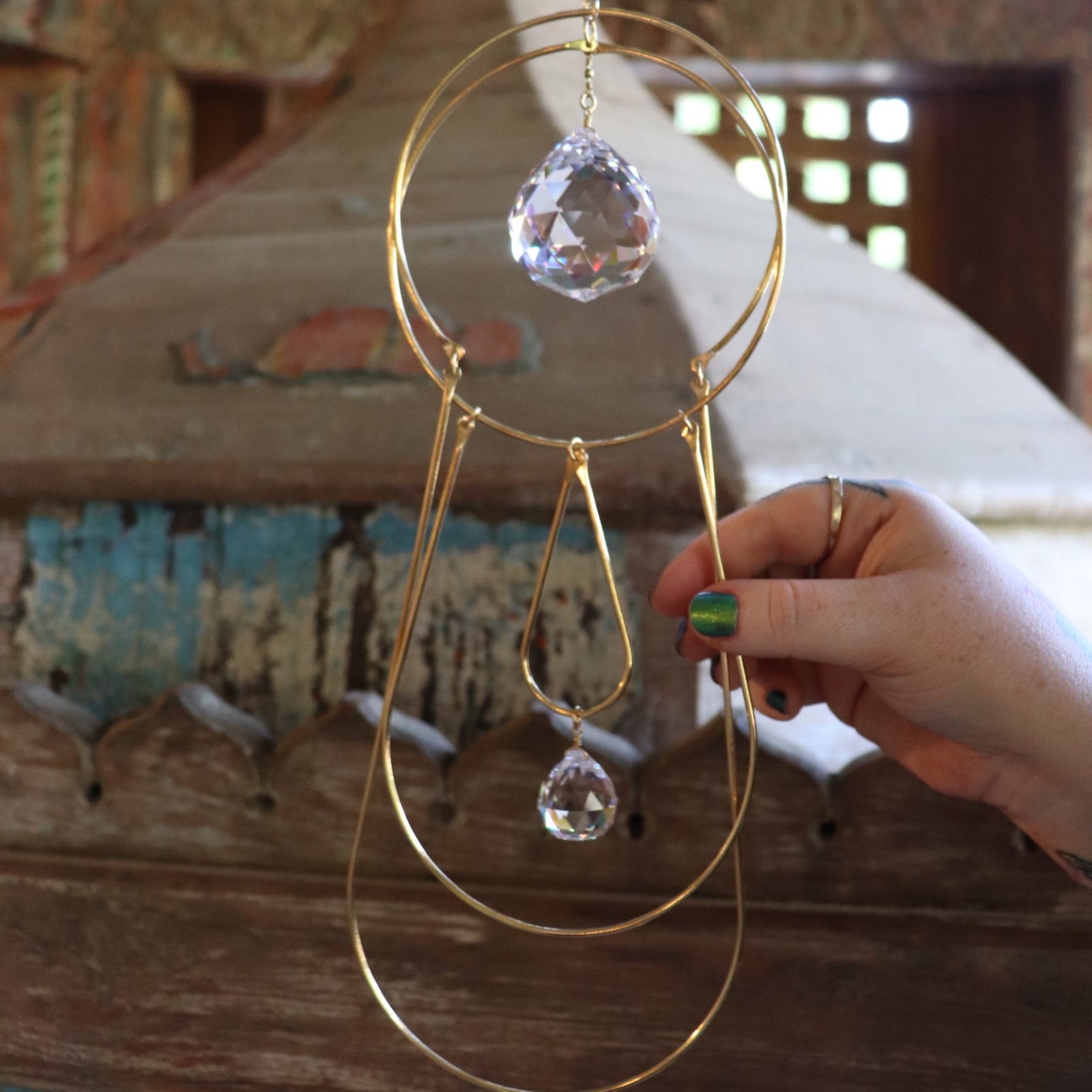 Someone holding the Prisma Hanging #43 Brass Suncatcher in front of a wooden altar.
