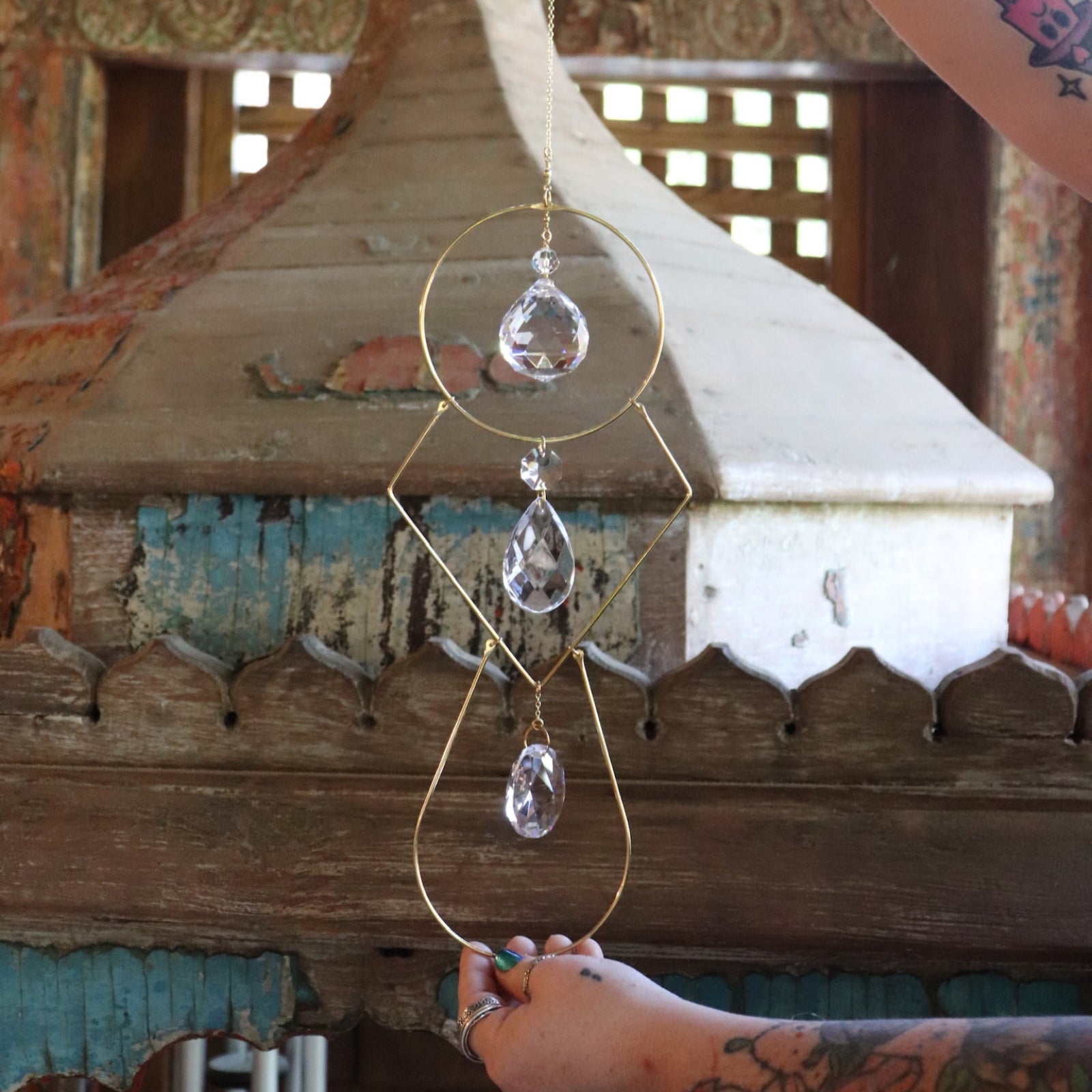 Someone holding the Prisma Hanging #42 Brass Geometrical Suncatcher in front of a wooden background.