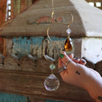 Someone holding the Prisma Hanging #35 Brass Suncatcher in front of a wooden background.