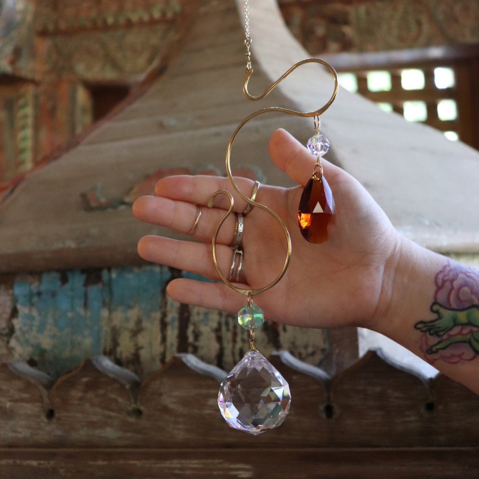 Someone holding the Prisma Hanging #35 Brass Suncatcher in front of a wooden background.
