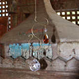 Someone holding the Prisma Hanging #35 Brass Suncatcher in front of a wooden background.