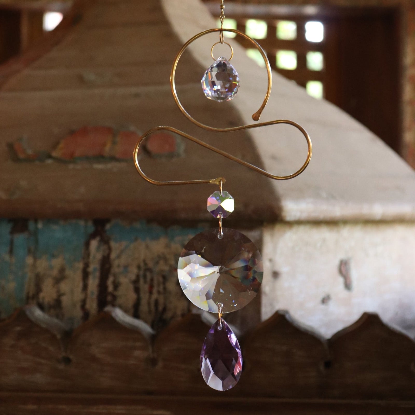 Someone holding the Prisma Hanging #36 Brass & Purple Suncatcher in front of a wooden background.