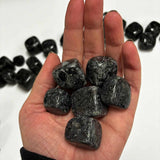 Hand holding several polished Indigo Gabbro tumbled stones in shades of deep gray and black