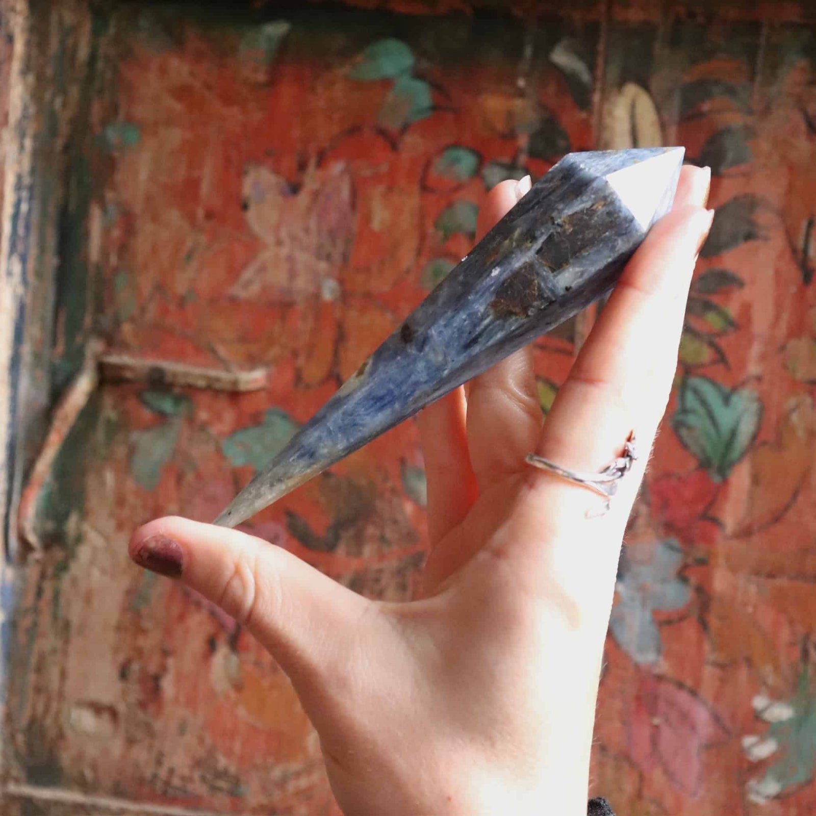 Hand holding a blue kyanite crystal against a colorful, textured background