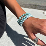 Hand wearing multiple Larimar beaded bracelets on a blurred outdoor background
