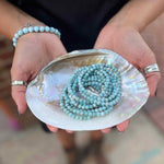 Person holding a shell with a Larimar beaded bracelet inside, wearing bracelets and rings.
