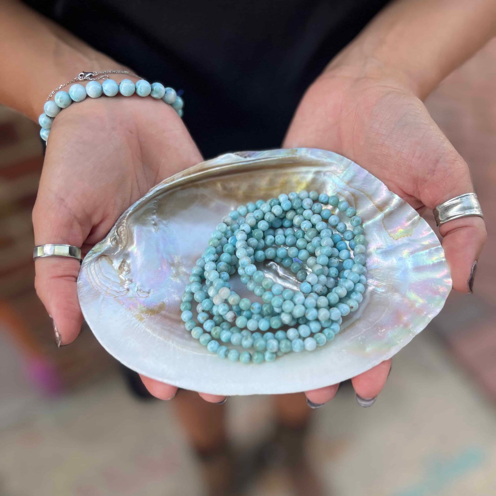 Person holding a shell with a Larimar beaded bracelet inside, wearing bracelets and rings.