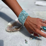 Hand wearing multiple Larimar beaded bracelets on a light surface