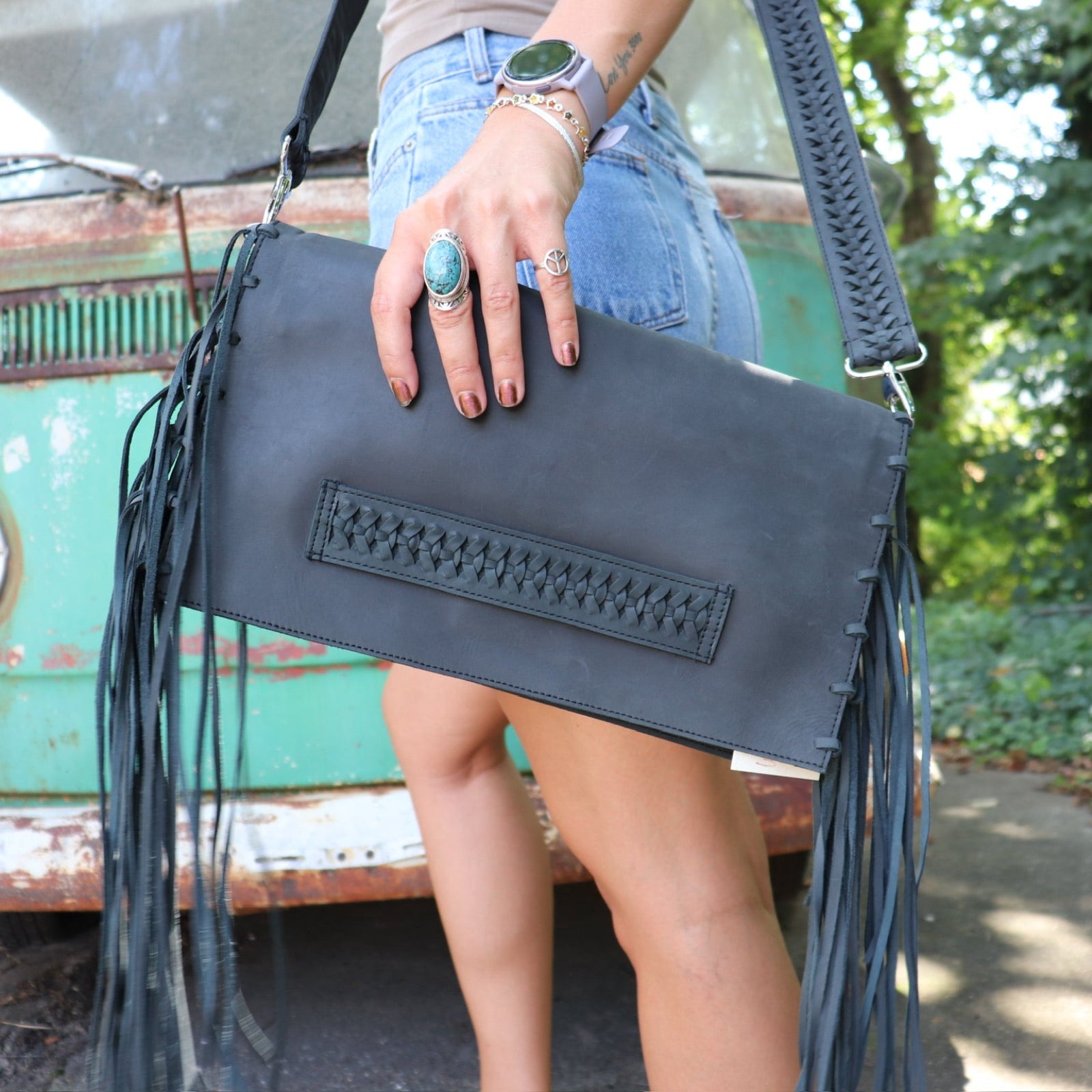 Person holding a black leather clutch with fringe details in front of a vintage green van.