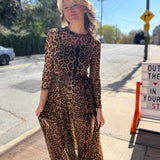 leopard mesh dress on model standing in front of orange and pink building model smiling holding both sides of dress 