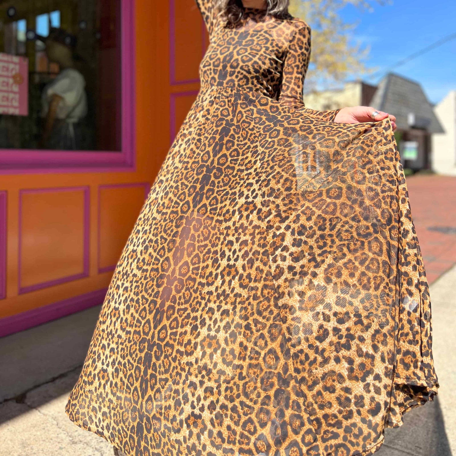 leopard mesh dress on model standing in front of orange and pink building holding skirt out looking down on dress