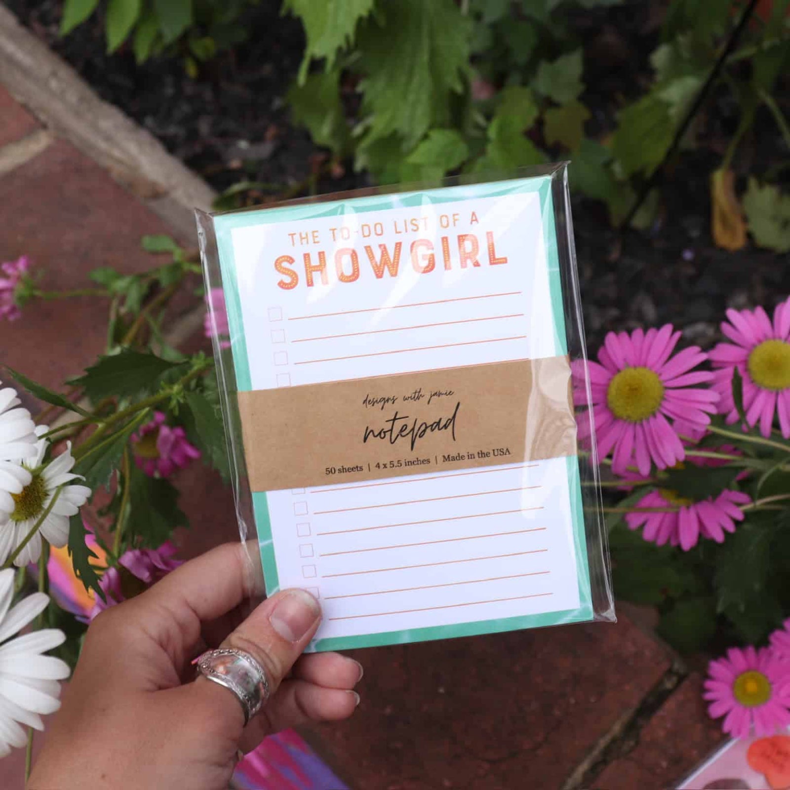 Hand holding a notepad with 'She is a Showgirl' text against a floral background