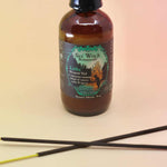 up close image of the litha sea witch botanicals spray with 2 crossed incense sticks on an orange and pink background