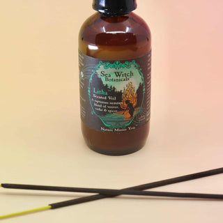 up close image of the litha sea witch botanicals spray with 2 crossed incense sticks on an orange and pink background