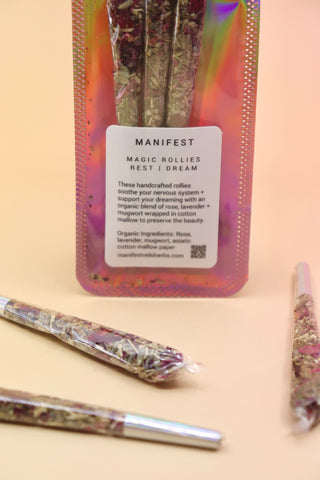 Holographic package of Manifest Magic Rollies with visible herbs inside, surrounded by individual rollies on a soft blush background