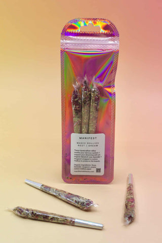 Holographic package of Manifest Magic Rollies with visible herbs inside, surrounded by individual rollies on a soft blush background