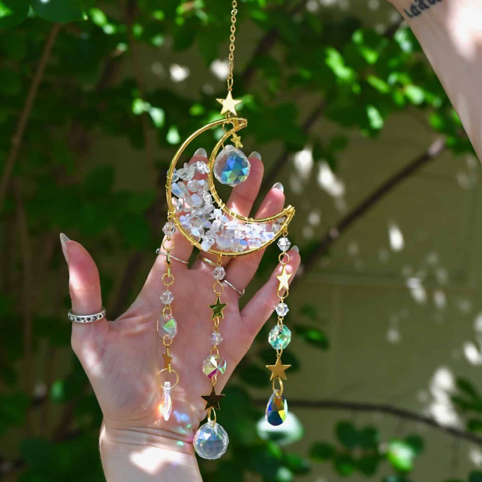 Decorative hanging ornament with beads and gemstones held by a hand against a green leafy background