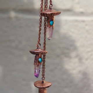 Copper mushroom necklaces with Vera Cruz Amethyst and turquoise teardrops hanging against stone wall