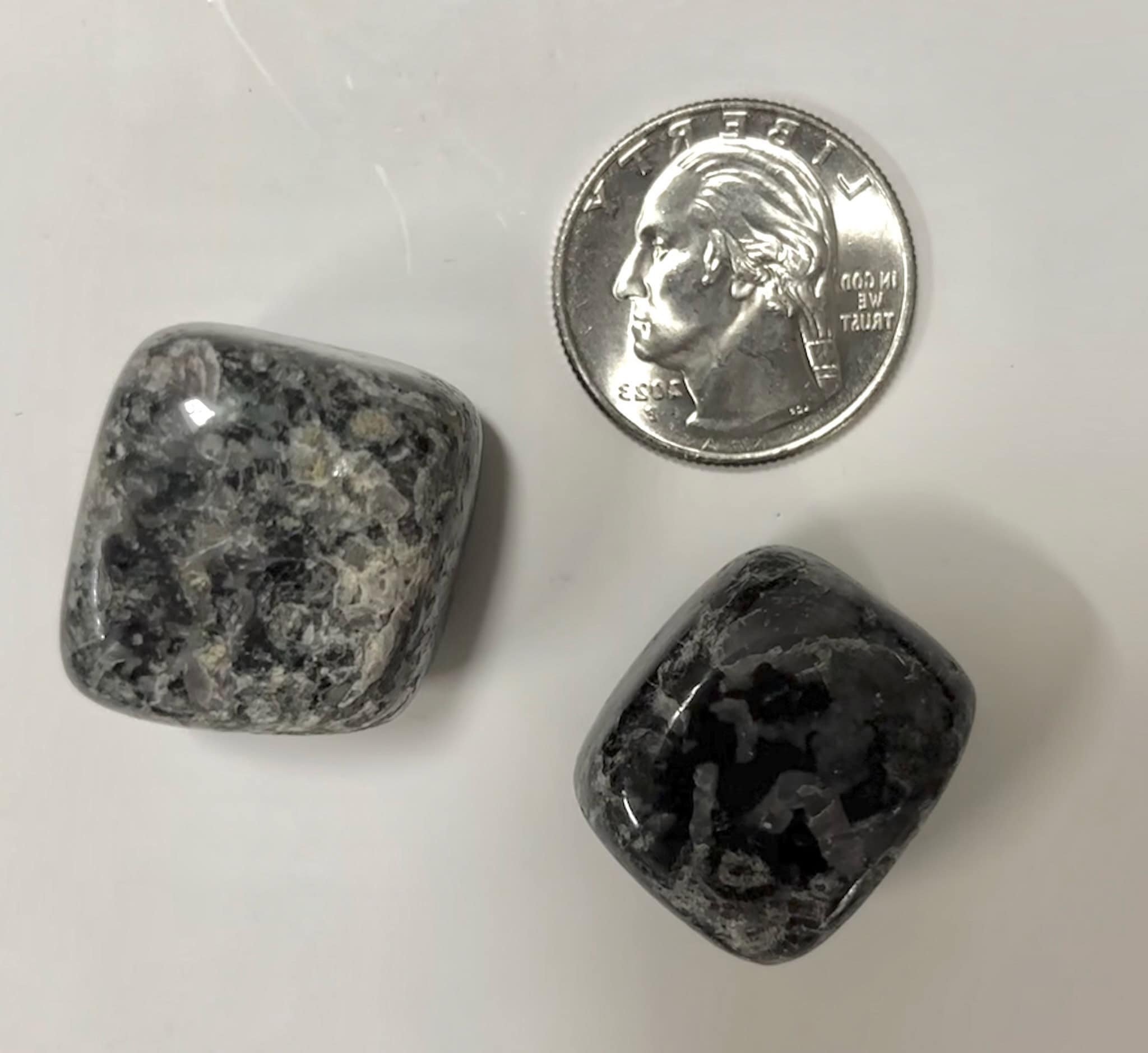 Two Indigo Gabbro tumbles next to a quarter to show size