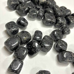 Dozens of polished Indigo Gabbro tumbles scattered across a white surface