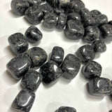 Dozens of polished Indigo Gabbro tumbles scattered across a white surface