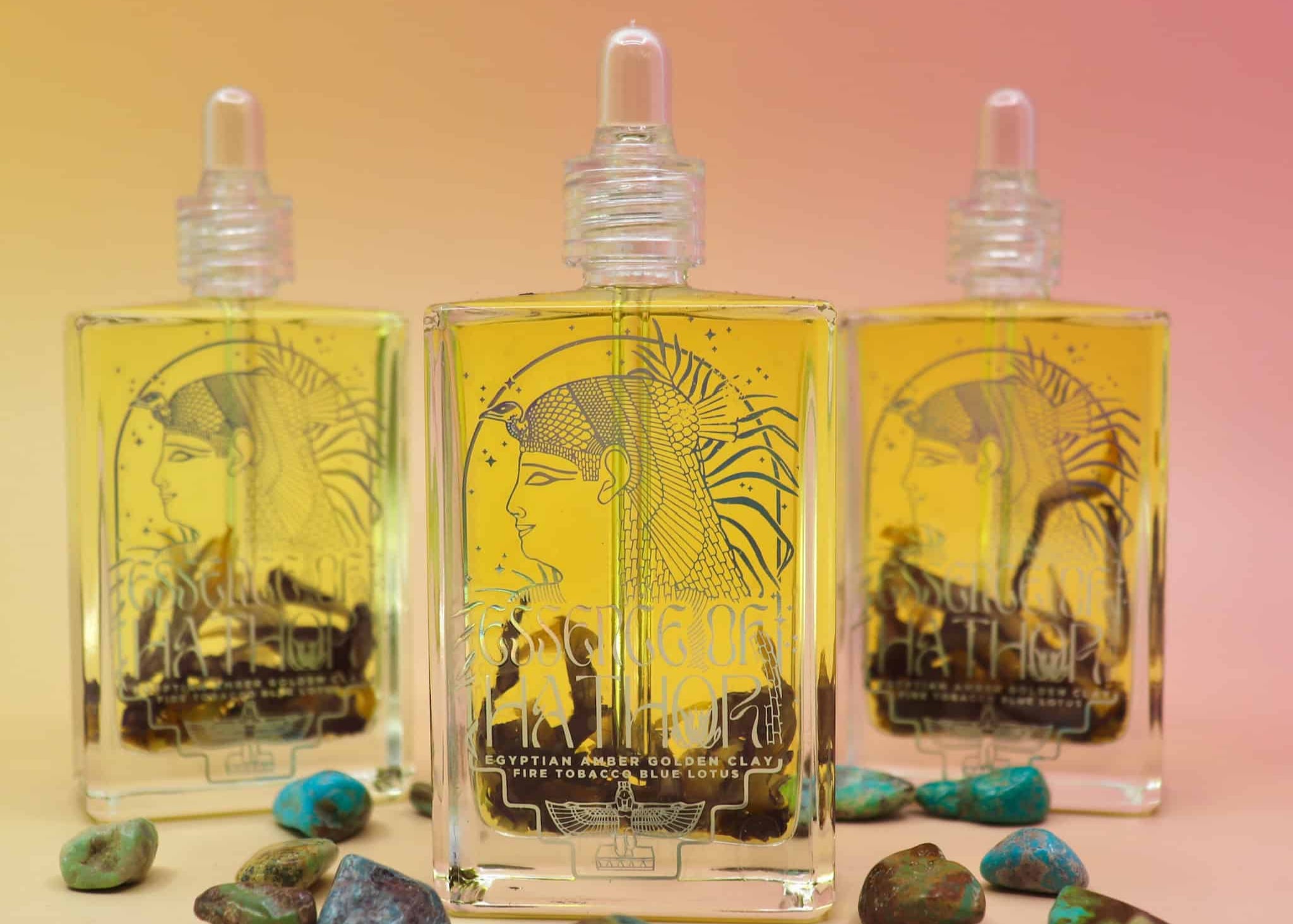 Three glass bottles with Egyptian-themed labels and turquoise stones on a gradient background