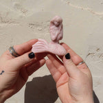Pink opal crystal mermaid sculpture of a figure held between two hands against a beige background