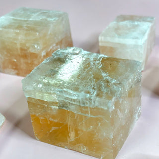 Raw optical calcite cube with glowing golden hue on pink background