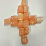 orange selenite tumbles arranged in a cross formation, showcasing color variation