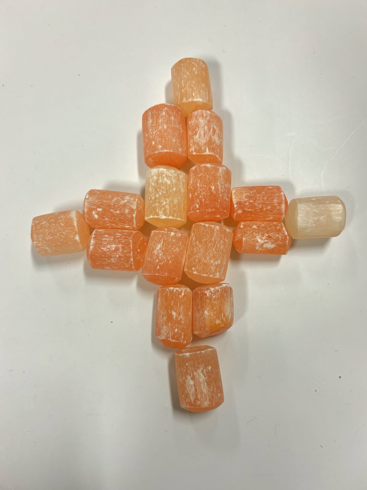 orange selenite tumbles arranged in a cross formation, showcasing color variation