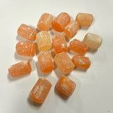 Group of polished orange selenite cylinder tumbles scattered on white background