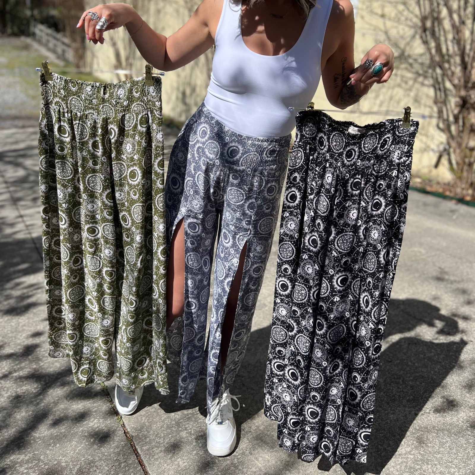 Someone wearing the gray Celestial Faux Wrap Pants while also holding up the sage and black Celestial Faux Wrap Pants.