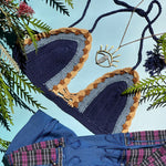The navy Festive Crochet Top: One Size on a blue background with blue pants, an evil eye necklace, and green stems surrounding the top.