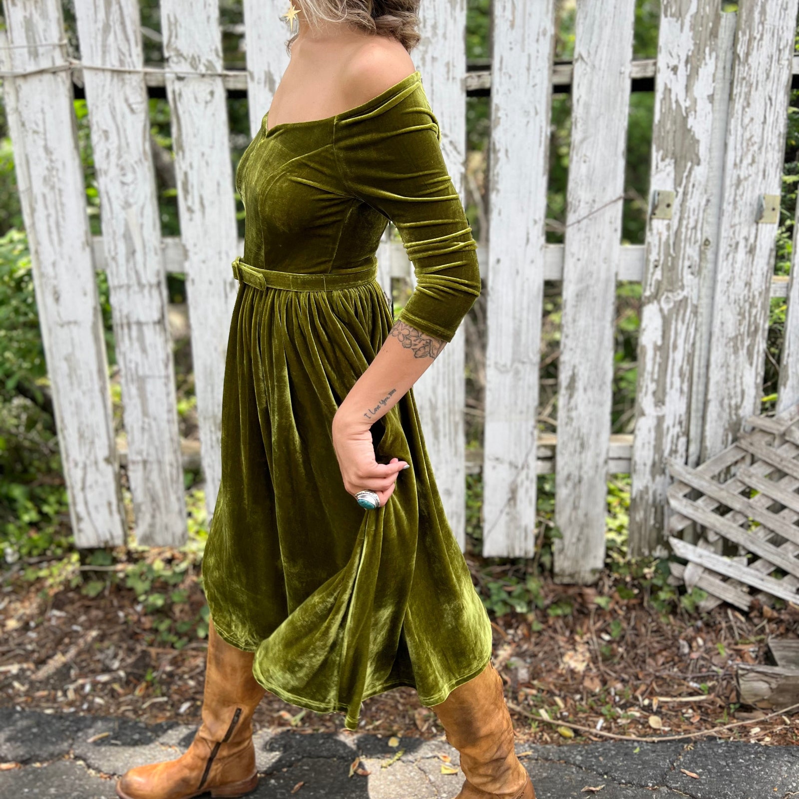 A woman wearing the 1950s Chartreuse Velvet Sweetheart Swing Dress in front of a wooden fence, showing off the side.