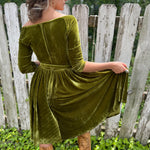 A woman wearing the 1950s Chartreuse Velvet Sweetheart Swing Dress in front of a wooden fence, showing off the back.