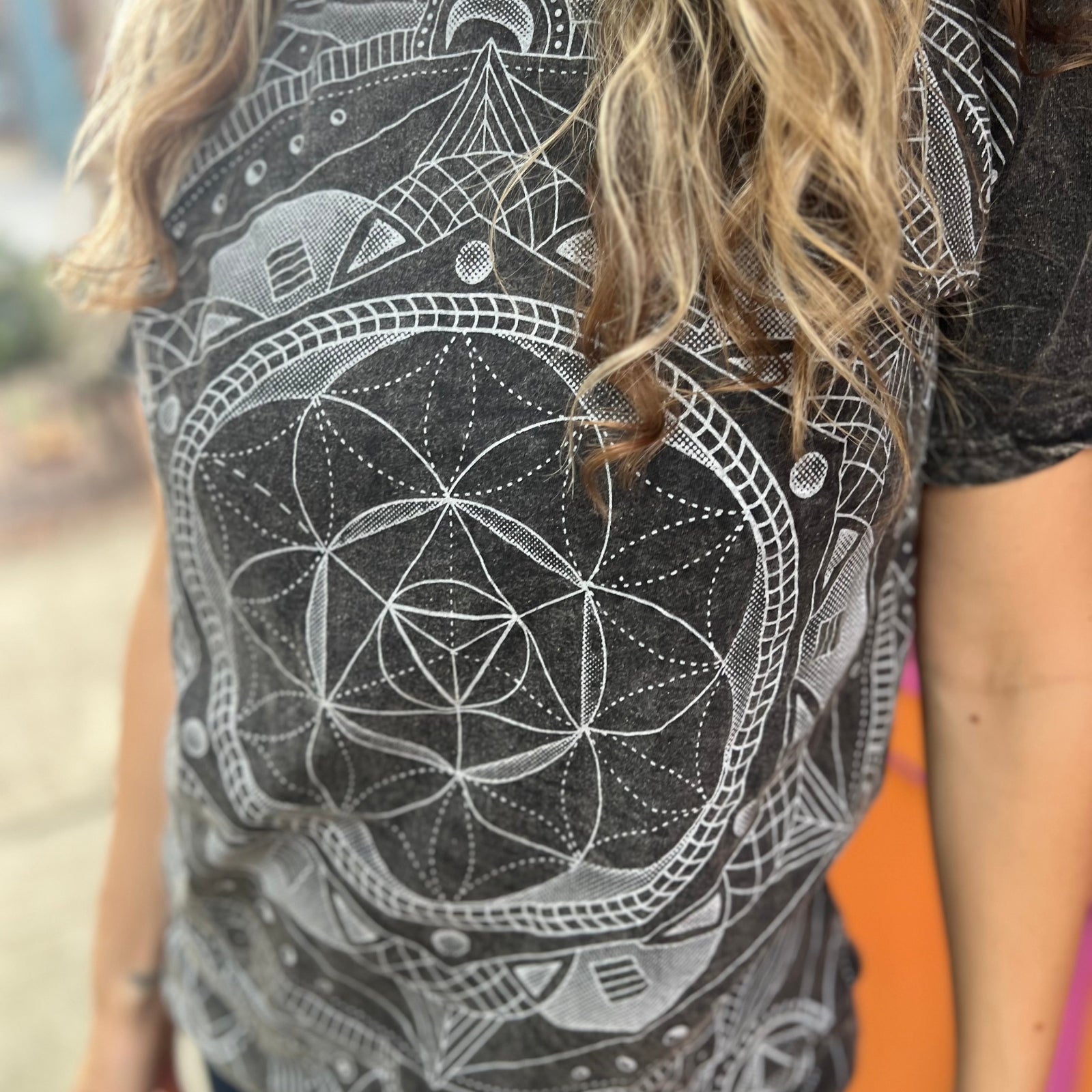 A woman wearing the Gray Mandala Stonewashed Cotton T-shirt with jeans in front an orange and pink wall.