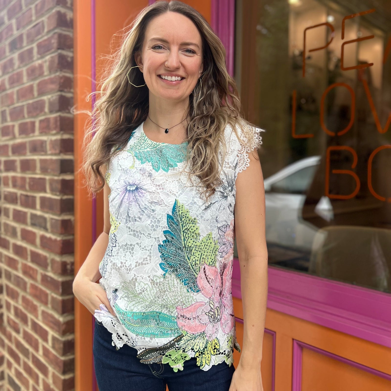 A woman wearing the Butterfly Lace Embroidered Trim Short Sleeve Top in front of an orange and pink wall.