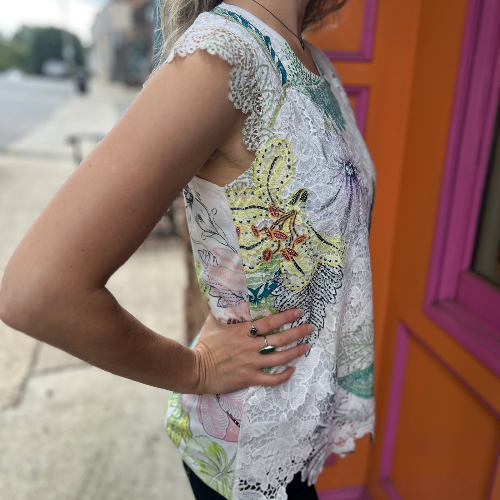 A woman wearing the Butterfly Lace Embroidered Trim Short Sleeve Top in front of an orange and pink wall.